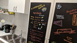 Eine Küche mit einer Kreidetafel, auf der eine Speisekarte mit Rezept für Spaghetti Carbonara, einschließlich Zutaten und Zubereitung, aufgelistet ist.