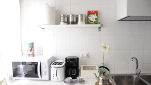 Eine Küche mit Mikrowelle, Toaster, Kaffeemaschine und Spüle. Es gibt außerdem Regale mit Gläsern und eine Vase mit einer Blume.