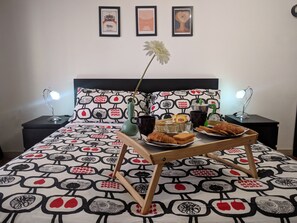 A neatly made bed with a patterned bedspread, a bedside table with a lamp, and a tray with food and drinks on the floor. - Kokoroma Apartment Vatican area Rome (Roma)