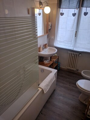 A bathroom with a bathtub, a sink, and a toilet. There is a window with curtains and a mirror above the sink. - Kokoroma Apartment Vatican area Rome (Roma)