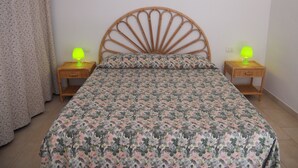 Una cama con colcha estampada, dos mesitas de noche con lámparas y una cortina.