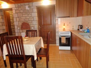 A cozy kitchen with a stone wall, wooden cabinets, a stove, and a dining area with chairs and a table.