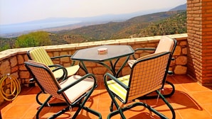 Una terraza con una mesa y cuatro sillas, con vista a un paisaje montañoso.