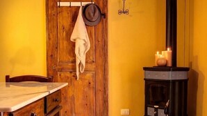 A rustic room with a wooden door, a table with a chair, a stove with candles, and a hat hanging on the door.