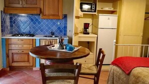 A compact kitchen with a stove, sink, and microwave. There is a dining table with chairs and a red blanket on the bed.