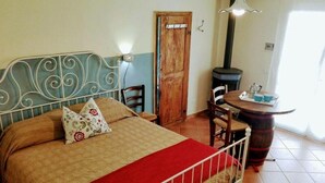 A bedroom with a bed, a wooden door, a round table with chairs, and a small stove.