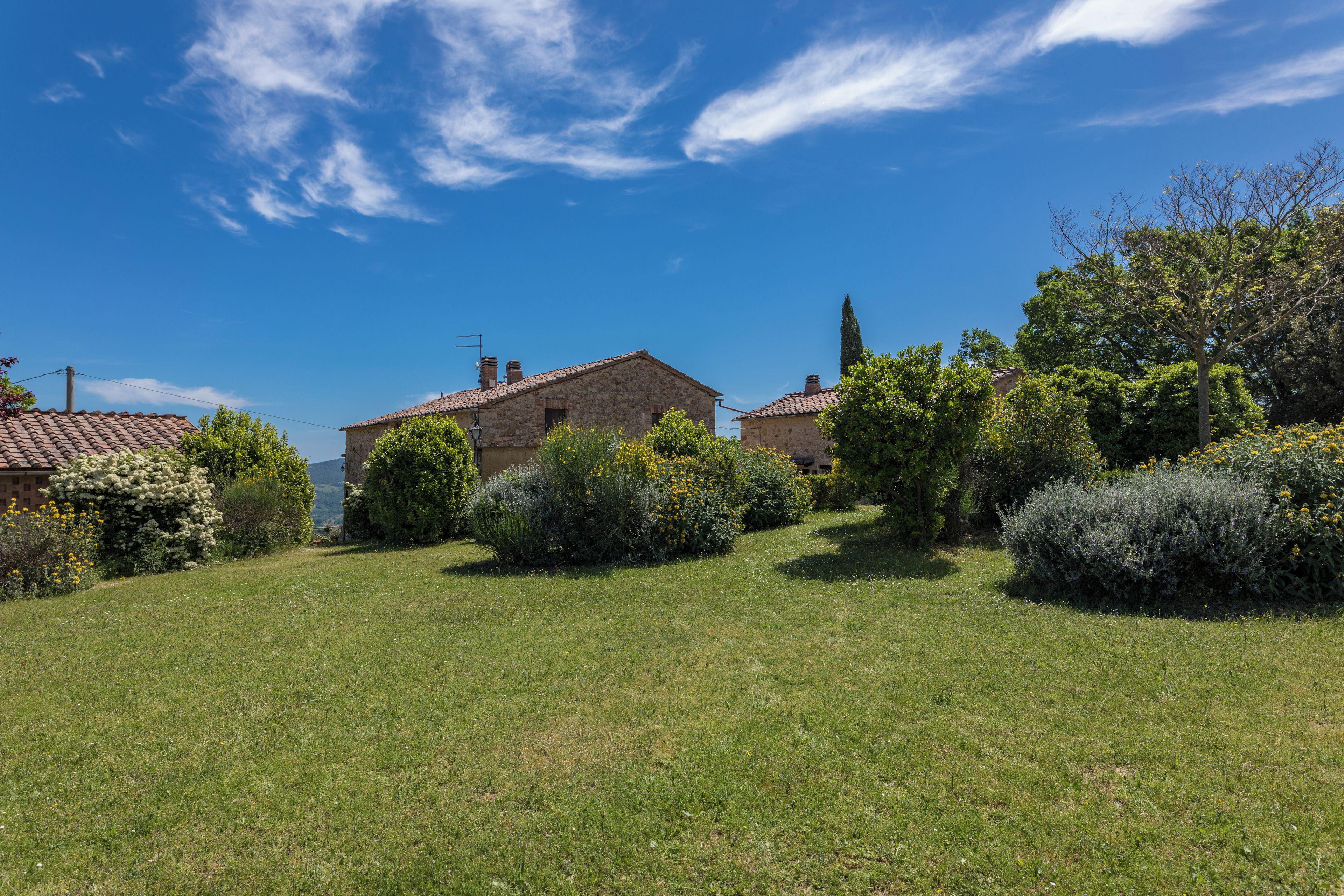A rural landscape with a stone house, lush greenery, and a clear blue sky.