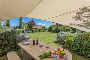 Ein Essbereich im Freien mit einem Tisch für zwei Personen, komplett mit Weinflaschen, Gläsern und einem Korb mit Obst und Brot.