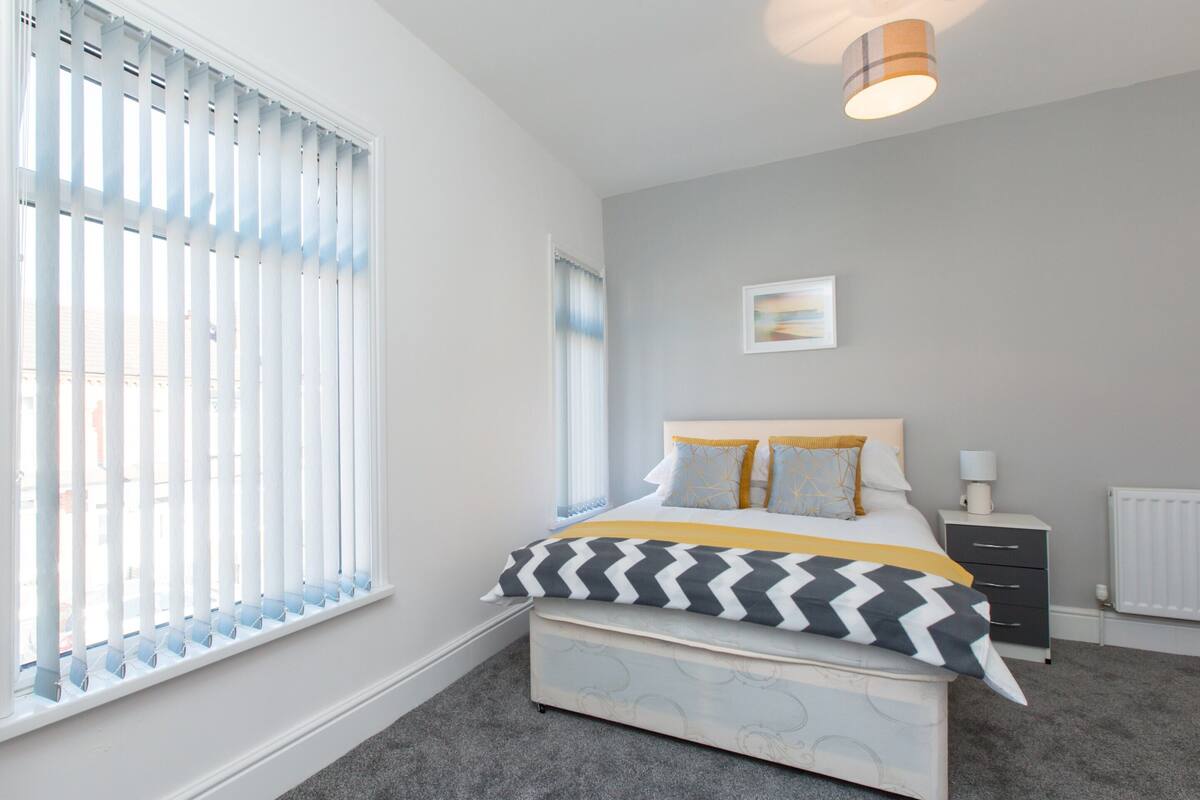 A bedroom with a bed, bedside table, and a window with blinds.