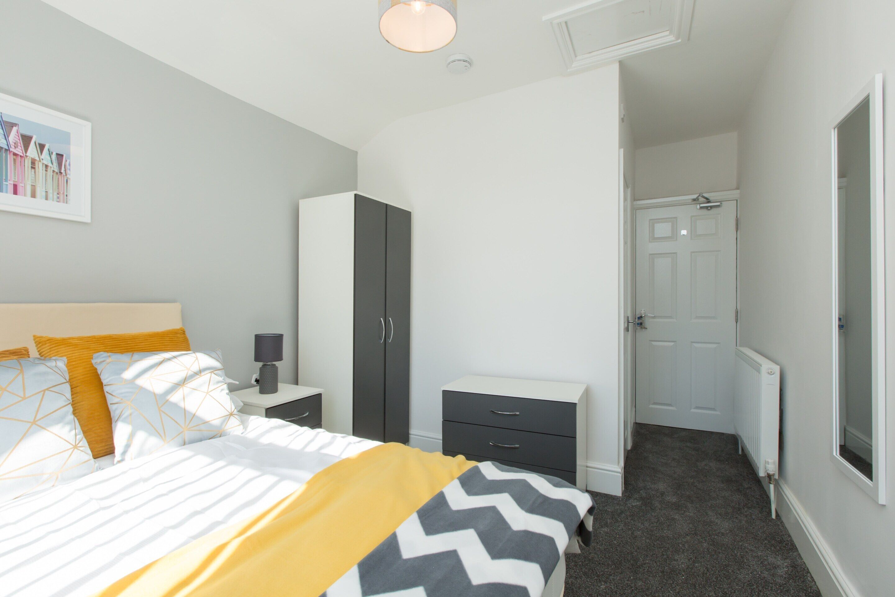 A bedroom with a bed, a wardrobe, a nightstand, and a door leading to another room.