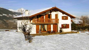 Un chalet de dos pisos con balcón, contraventanas de madera y un paisaje cubierto de nieve.