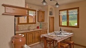 Una cocina con armarios de madera, un ventanal con vista a la vegetación y una mesa de comedor lista para dos comensales.