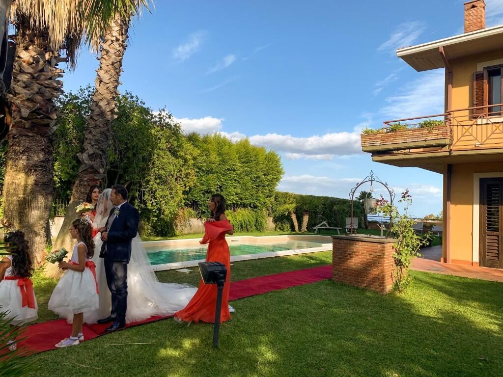 A wedding ceremony with a red carpet, palm trees, and a pool in the background.