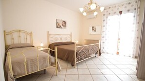 A bedroom with two beds, a chandelier, and a large window with curtains.