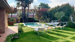 A pool area with lounge chairs, a brick building, and palm trees.