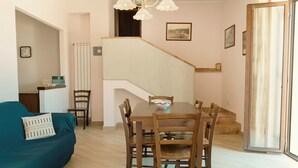Un comedor con mesa y sillas de madera, una escalera, un sofá y un reloj en la pared.