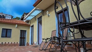 Un edificio con patio empedrado, sillas de metal y un balcón.