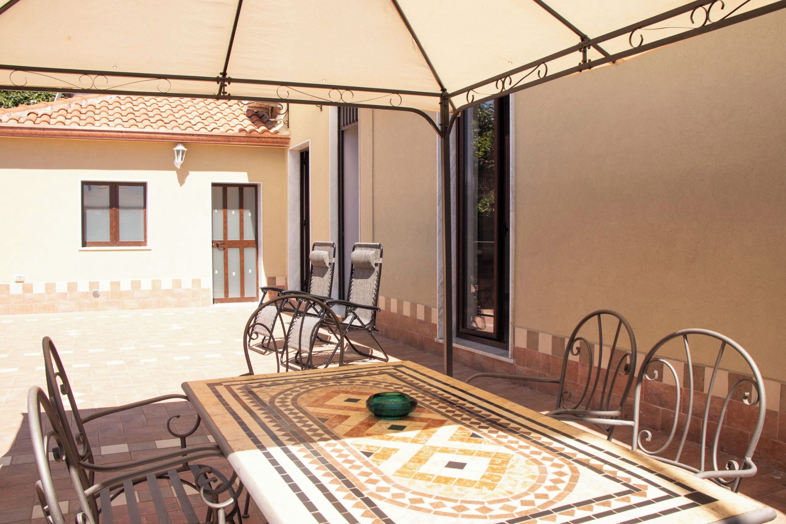 Une terrasse extérieure avec une table et des chaises, un espace abrité et un bâtiment en arrière-plan.