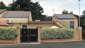 Un edificio con paneles solares en el techo, una entrada con portón y una escalera que lleva a un nivel superior.