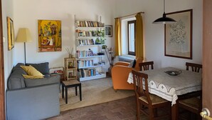 Una sala acogedora con un sofá, una mesita, una estantería y una mesa de comedor con sillas.