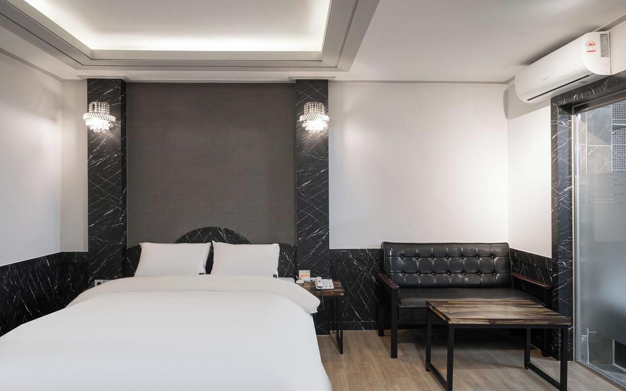 Quarto de hotel com cama, área de estar com mesa e uma janela grande.