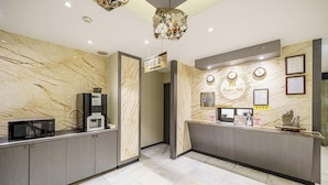 Un espace d’accueil avec des murs en marbre, un comptoir de réception, une horloge, des certificats encadrés et une machine à café.