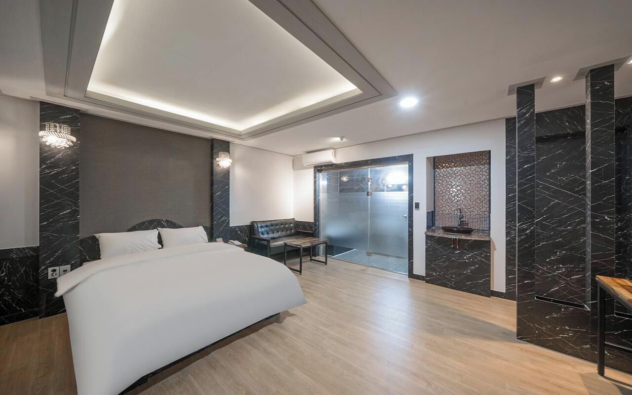 Un dormitorio moderno con una cama, un banco, una puerta de cristal y una pared de mármol.