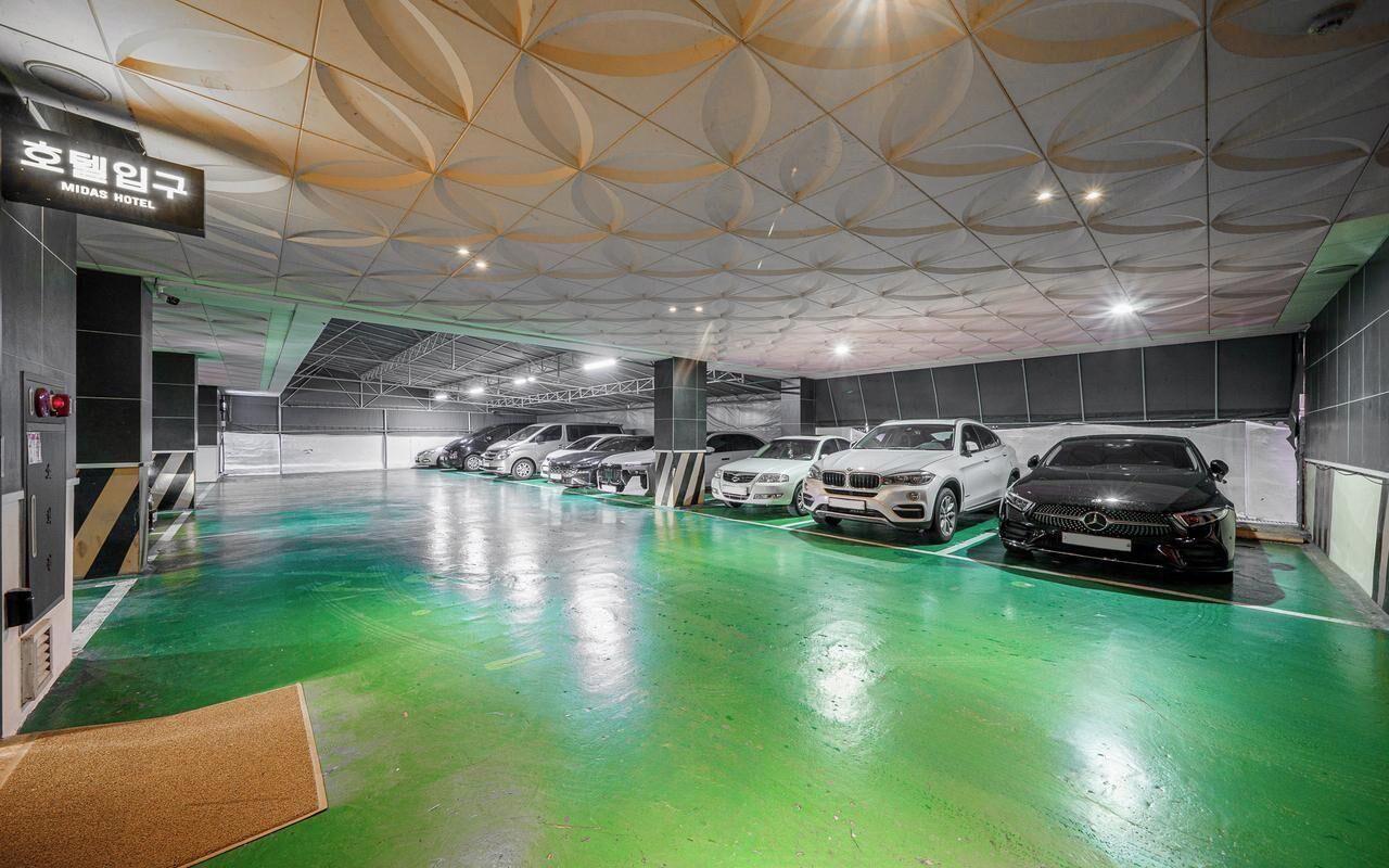 Uma garagem de estacionamento com vários carros, piso verde e teto com padrão geométrico.