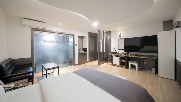 Une chambre d’hôtel moderne dotée d’un grand lit, d’un canapé, d’une télévision, d’un coin cuisine et d’une porte coulissante donnant sur un balcon.