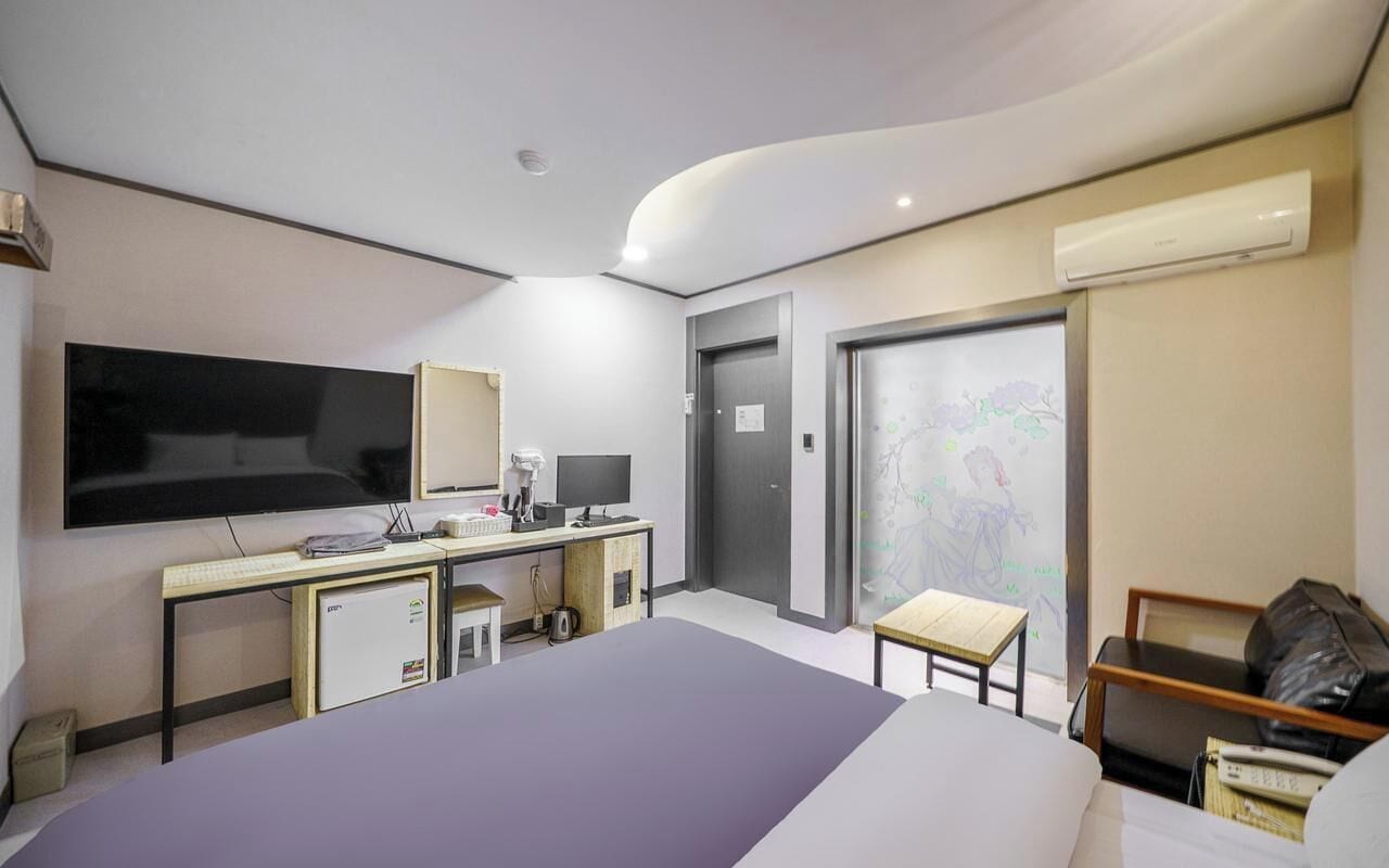 Una habitación de hotel moderna con una cama grande, un escritorio con computadora, un televisor de pantalla plana y una pequeña zona de estar.