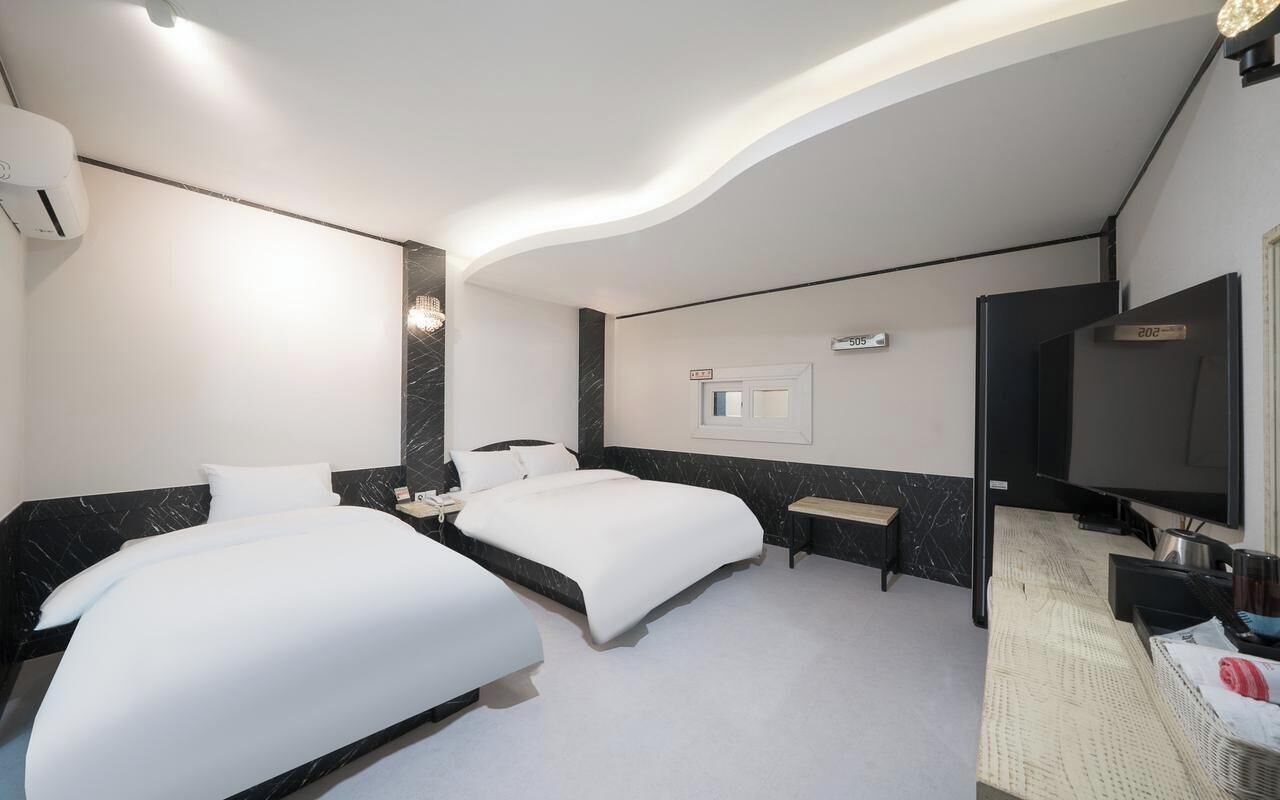 A hotel room with two beds, a TV, a desk, and a mirror.