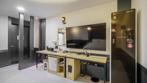 Une chambre d’hôtel moderne dotée d’une grande télévision à écran plat, d’un bureau en bois, d’un petit réfrigérateur et d’un ascenseur intégré.