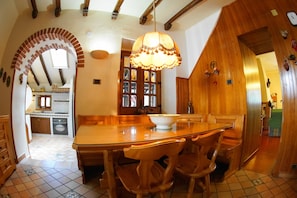 Un'ampia sala da pranzo con un tavolo e sedie in legno, un grande lampadario e vista sulla cucina.
