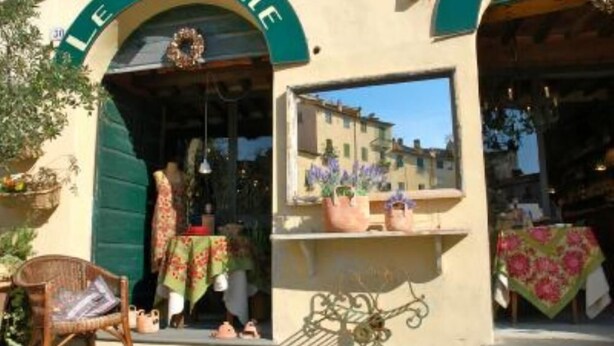 A storefront with a green awning, a wicker chair outside, and a table with a floral tablecloth. - Apartment in Amphiteatre Square inside the Walls (Lucca)