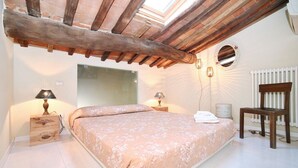 A bedroom with a large bed, wooden beams, a skylight, a mirror, a radiator, and bedside lamps. - Apartment in Amphiteatre Square inside the Walls (Lucca)