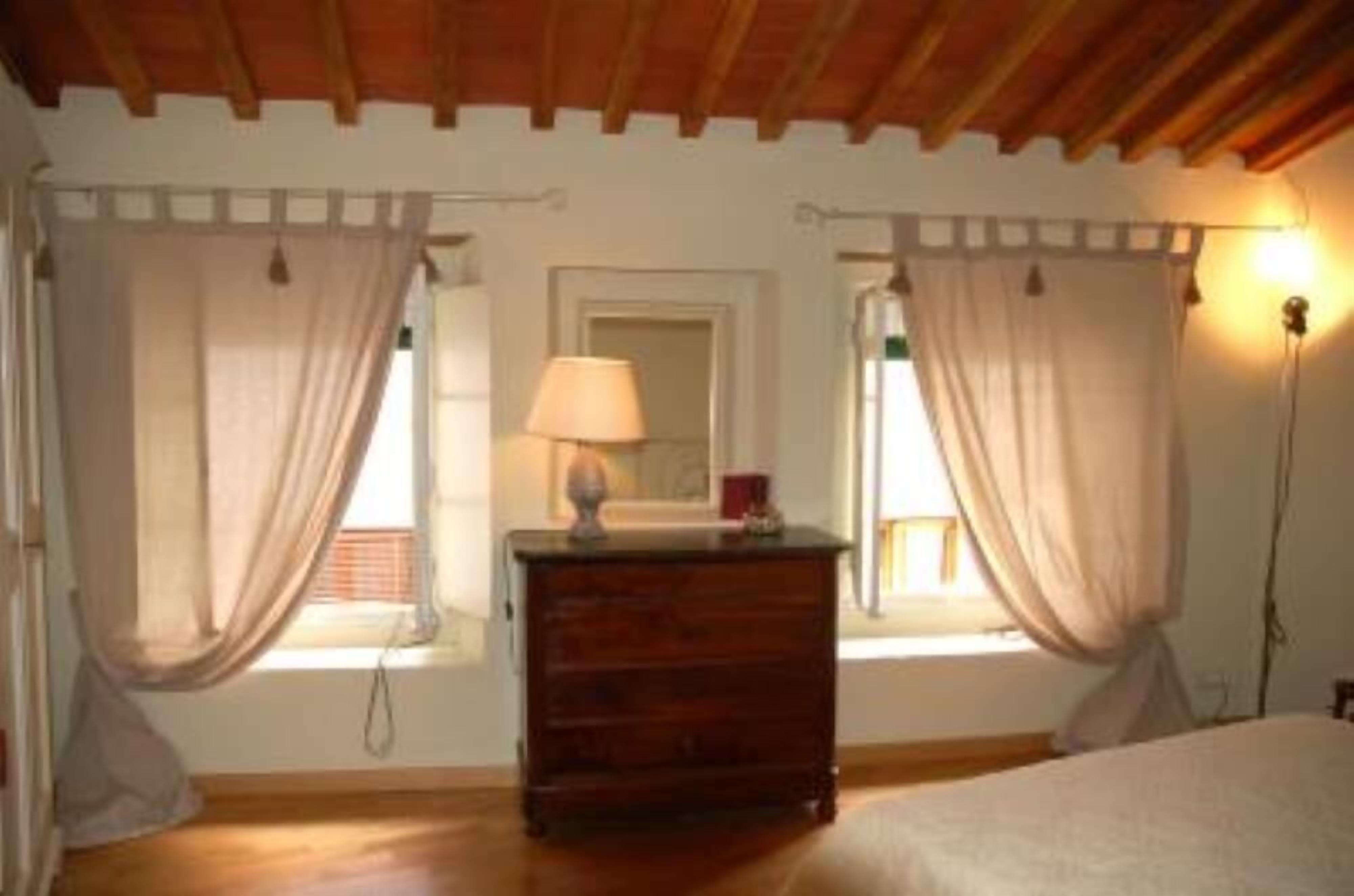 Un dormitorio con un aparador de madera, una lámpara y dos ventanas con cortinas.