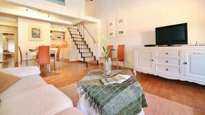 A spacious living area with a sofa, a dining table, chairs, a staircase, a television, and a cabinet. - Apartment in Amphiteatre Square inside the Walls (Lucca)