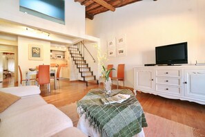 Uma sala ampla com sofá, mesa de jantar, cadeiras, escada, televisão e um armário.