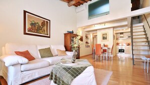 A spacious living room with a white sofa, a coffee table, and a staircase leading to an upper level. - Apartment in Amphiteatre Square inside the Walls (Lucca)
