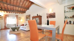 A dining area with a table and chairs, a sofa, a cabinet, and a window with curtains. - Apartment in Amphiteatre Square inside the Walls (Lucca)