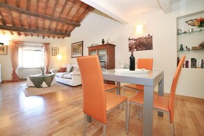Uma área de refeições com mesa, cadeiras, um sofá, um armário e uma janela com cortinas.