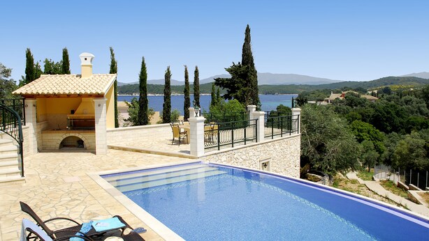 A swimming pool with lounge chairs and a barbecue area, overlooking a scenic landscape with trees and hills. - Villa Argyro (Corfu)