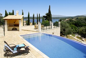 Piscina con sillas de descanso y zona de barbacoa, con vistas a un paisaje pintoresco con árboles y colinas.