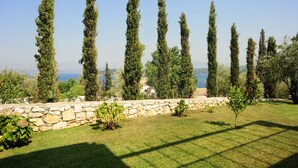 A stone wall with a grassy area and tall trees in the background. - Villa Argyro (Corfu)