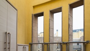 A balcony with yellow walls, a tiled floor, and a metal railing.