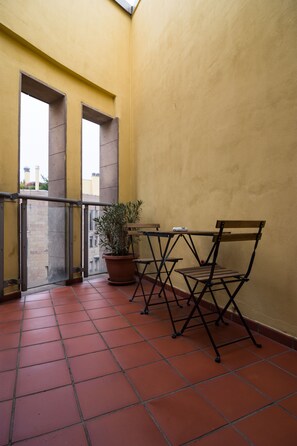 Ein Balkon mit gefliestem Boden, einem Blumentopf und einem Tisch mit Stühlen.