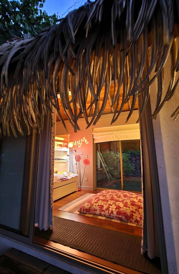 A cozy room with a bed, a small table, and a window with curtains. - Villa Meheana by Tahiti Homes (Maharepa)