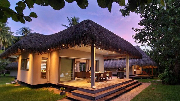 A modern house with a thatched roof, a covered patio, and a well-maintained lawn.