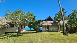 A resort with thatched-roof cottages, a grassy lawn, and a view of the ocean.