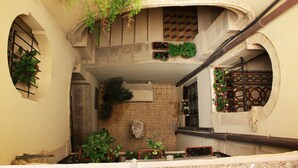 Un étroit escalier intérieur, fermé, avec un mur recouvert de carreaux, une petite fenêtre ornée d’une grille métallique et plusieurs plantes en pot.